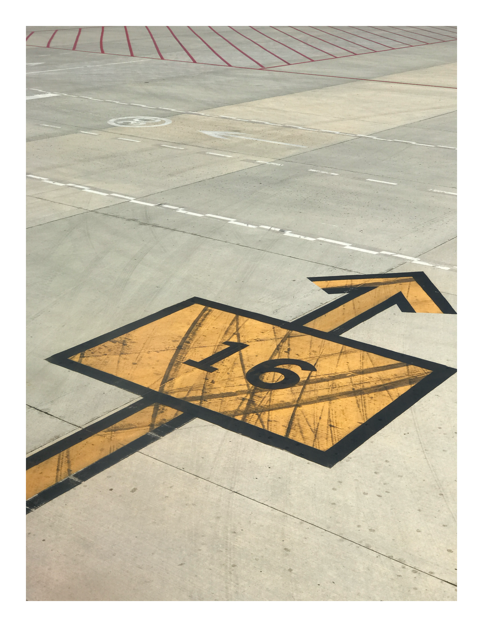 Painted directional arrow and the number 16 marked on an airport tarmac, with intersecting lines and worn concrete.