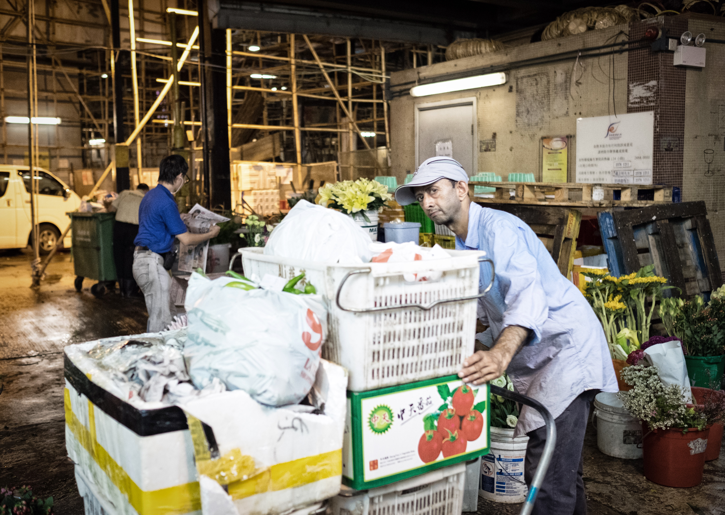Man pushing a cart of flowers and supplies in a market at night